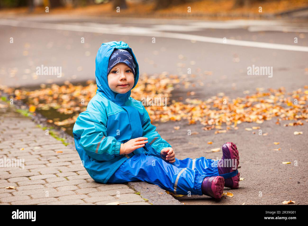 Happy child in waterproof coat and rainboots outdoors in autumn season. Stock Photo