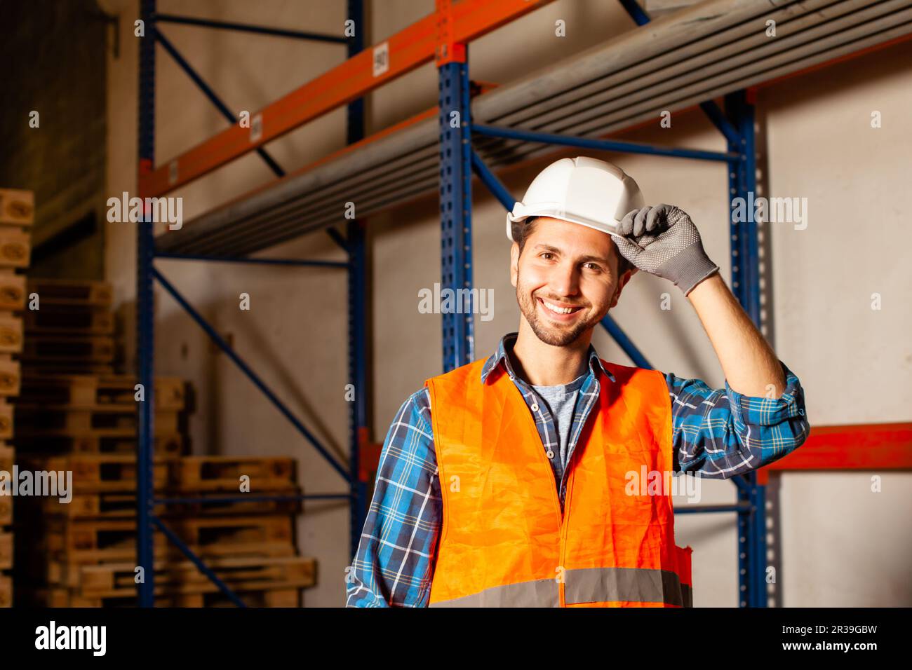 Confident handsome worker in protective hardhat and uniform at the warehouse of a industrial manufacturing Stock Photo