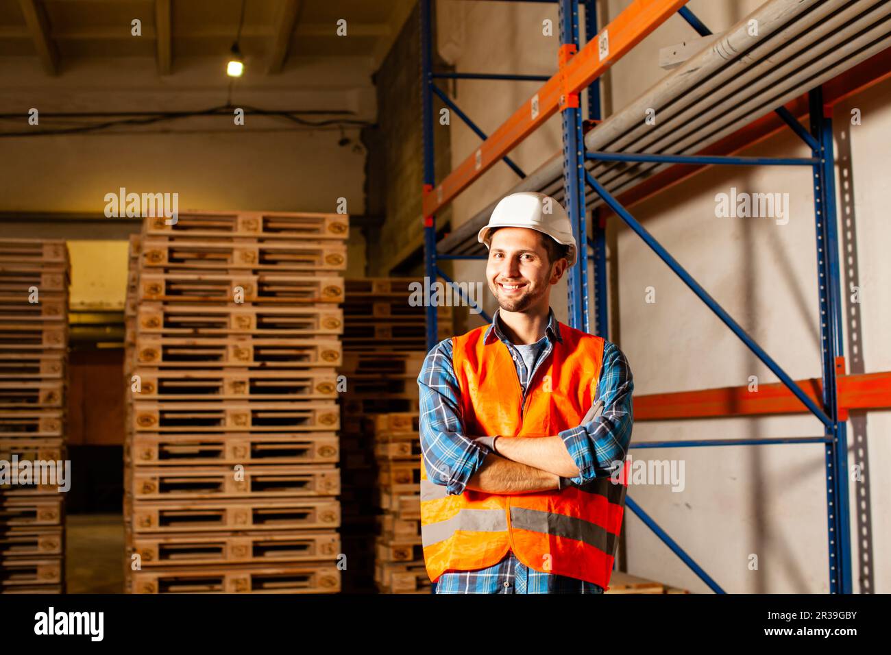 Happy young worker in protective uniform in front of wooden pallets Stock Photo