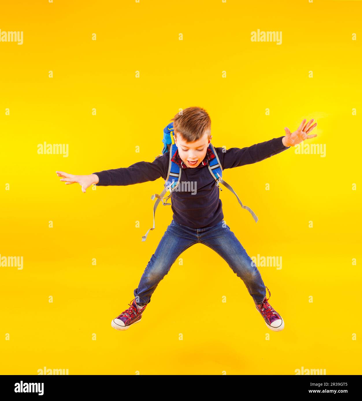 Happy kid jump with hand up. Cute exciting child boy ready to study with backpack isolated on yellow Stock Photo