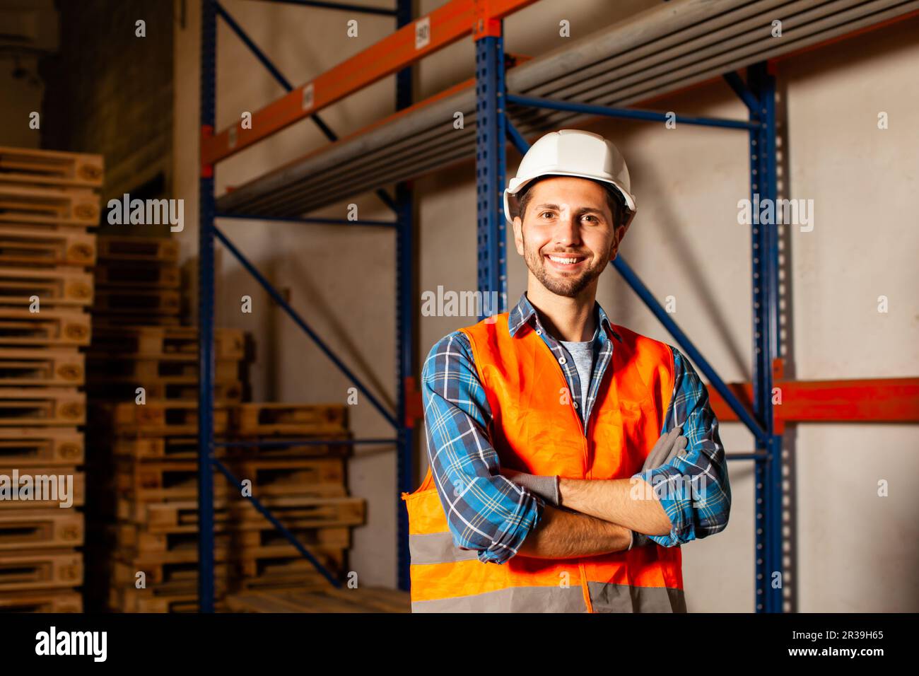 Confident handsome worker in protective hardhat and uniform at the warehouse of a industrial manufacturing Stock Photo