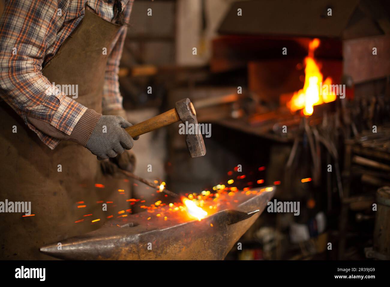 Blacksmith forging the molten metal on the anvil in smithy Stock Photo