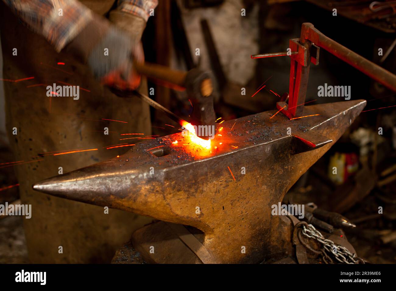 The blacksmith manually forging the molten metal on the anvil in smithy. Stock Photo