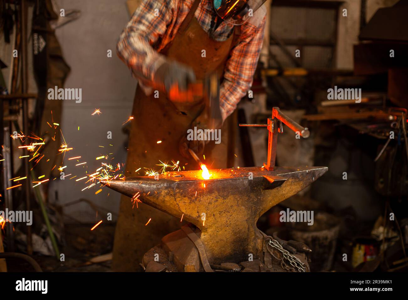 The blacksmith manually forging the molten metal on the anvil in smithy with spark fireworks. Stock Photo