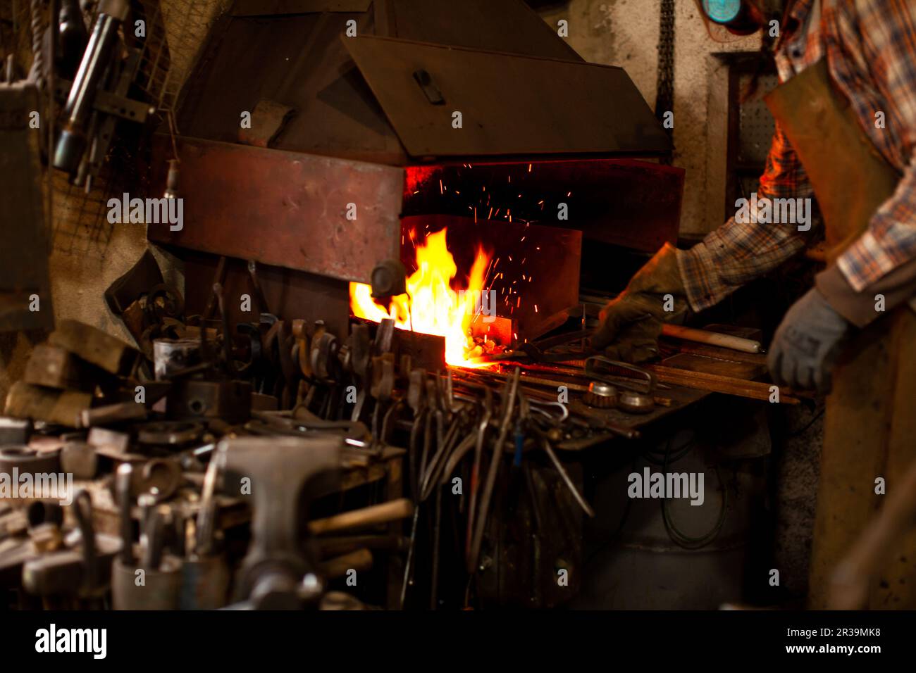 The blacksmith manually forging the molten metal on the anvil in smithy. Stock Photo