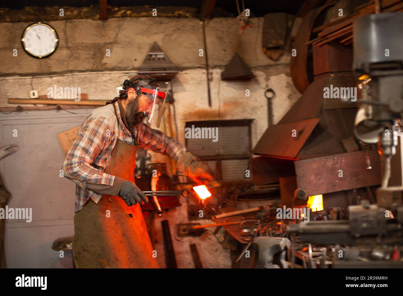 Real brutal blacksmith works in a workshop with a red-hot iron. Stock Photo