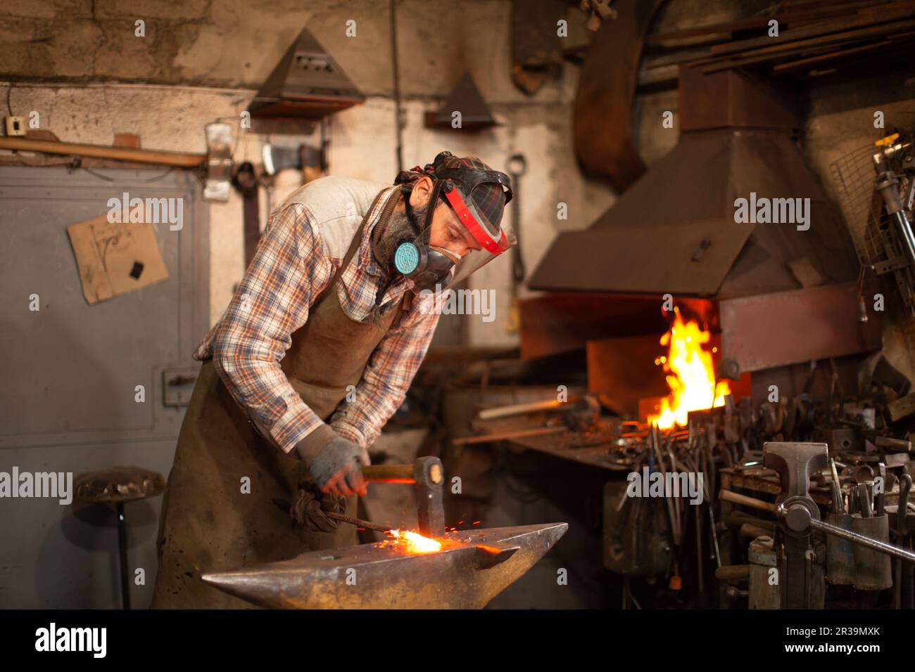 The blacksmith forging the molten metal on the anvil in smithy. Stock Photo
