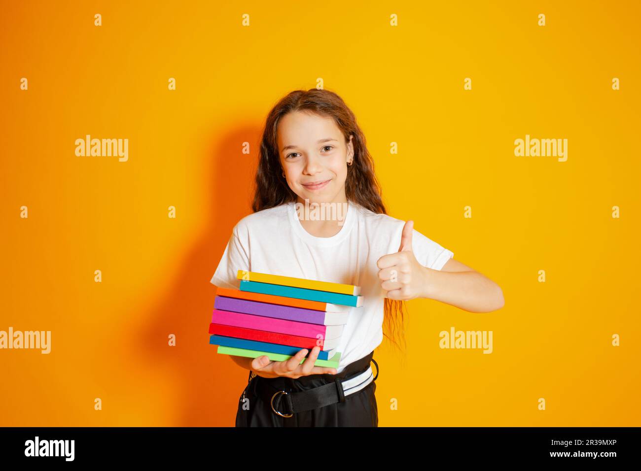 School girl holding stack of books over yellow background. Happy girl ...