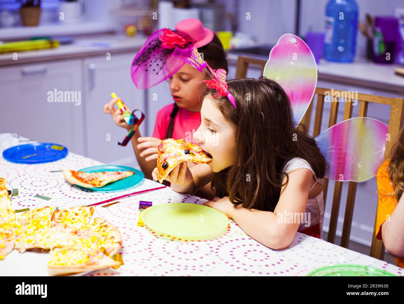 Cute little girl eats pizza at party. Pretty girl in butterfly costume. Birthday party Stock Photo