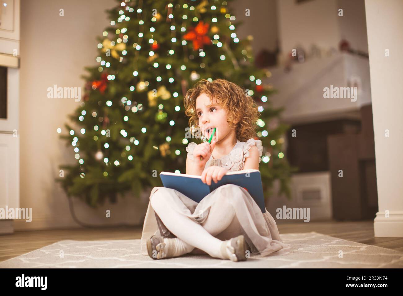 Dreamy girl sitting near decorated Christmas tree Stock Photo