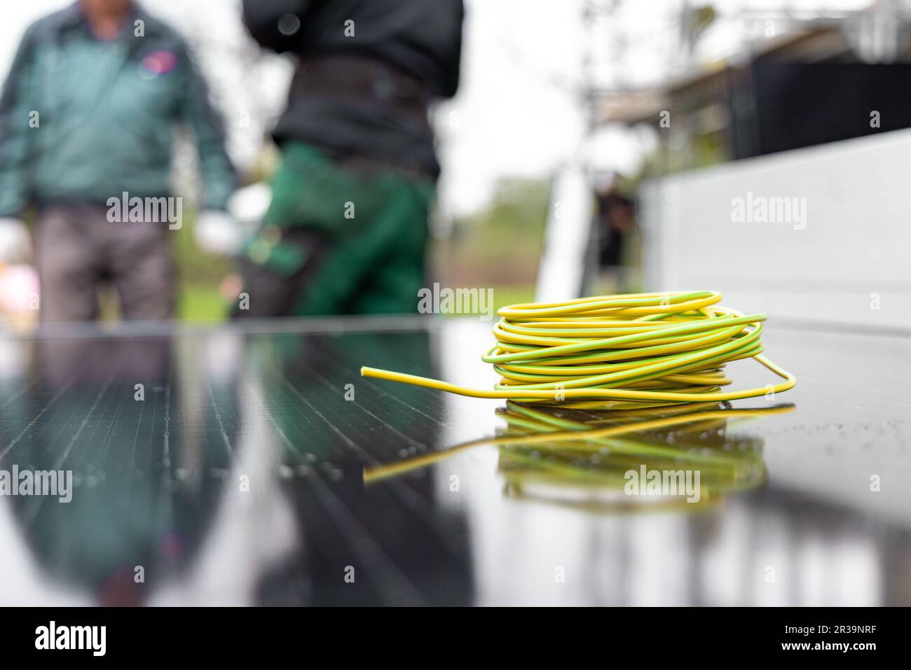 A coil of electric cable on a solar panel with technicians in the background Stock Photo