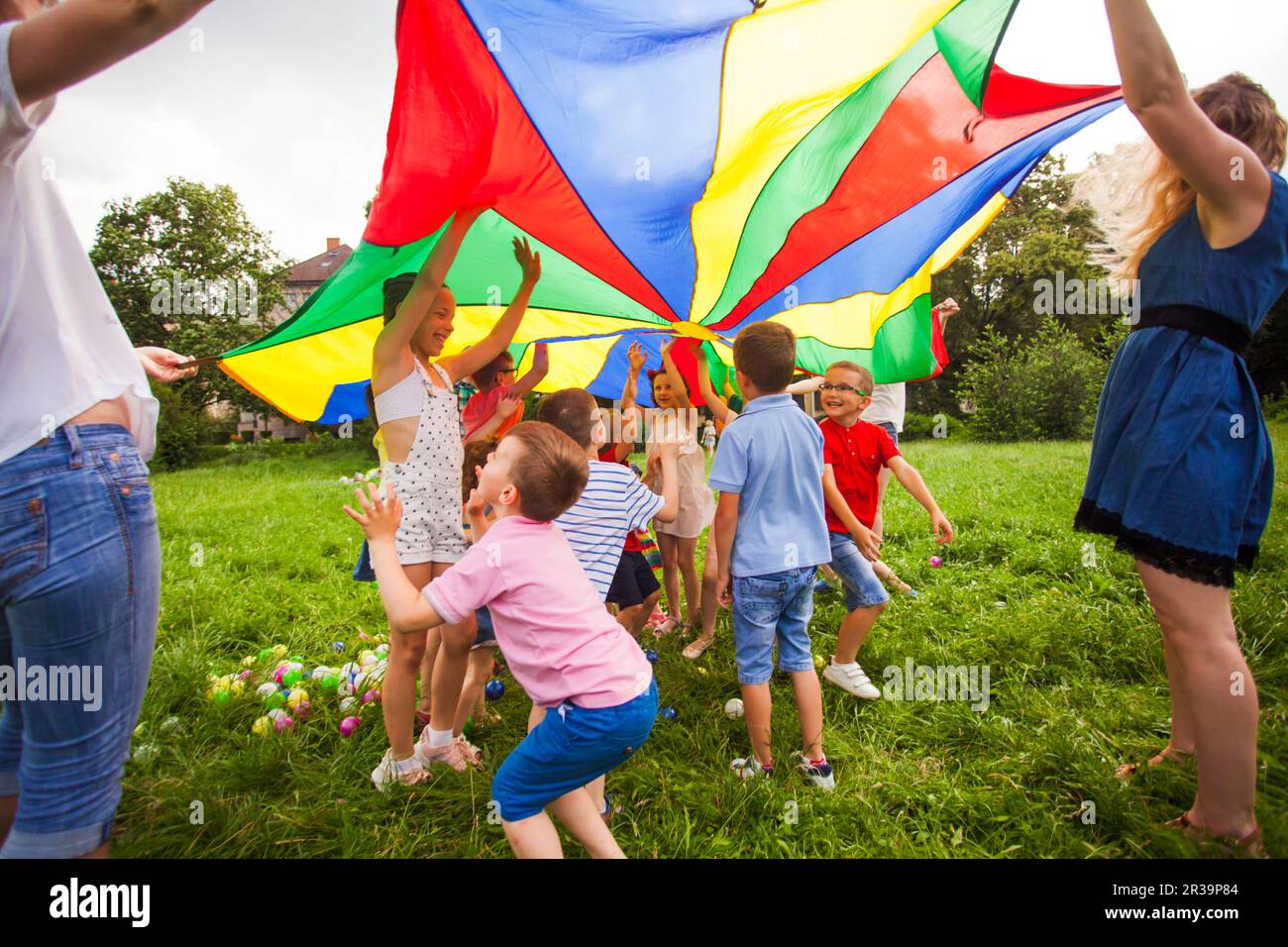 Kids hide under rainbow parachute outdoors game Stock Photo