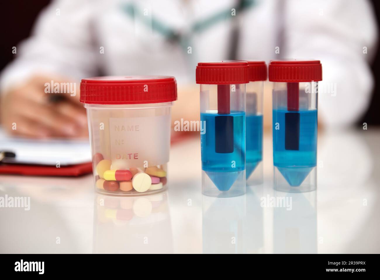 Woman Working In Clinic. Blue Sample And Tablet On table. Close Up Stock Photo