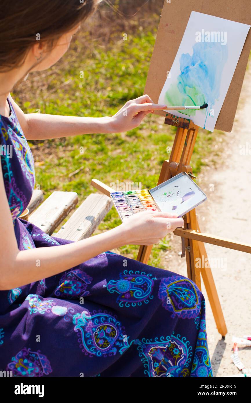 Girl is painting with watercolor on the easel outdoors. Spring imagination. Stock Photo