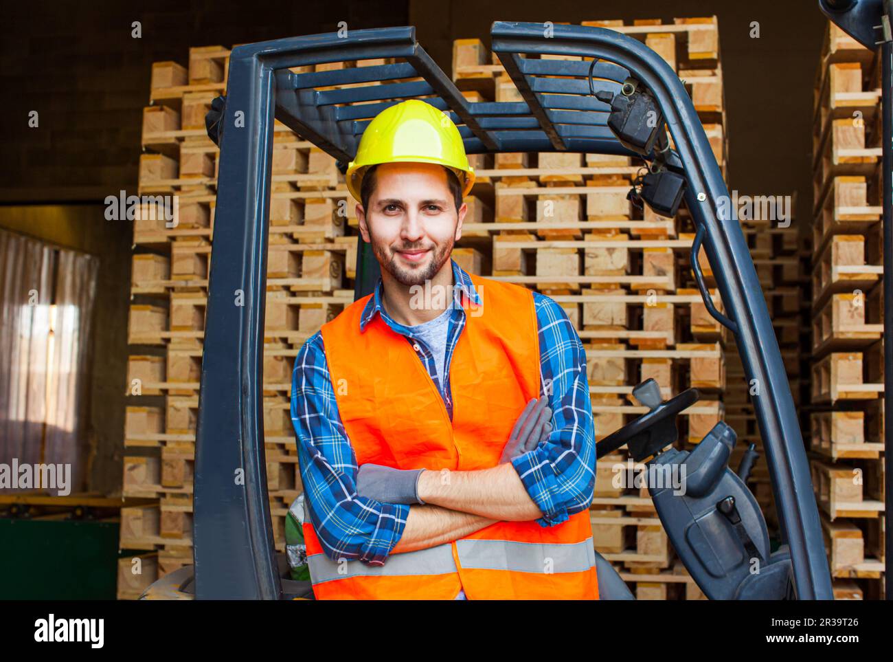 Handsome smiling worker driving forklift in warehouse. Woodworking industry concept. Stock Photo