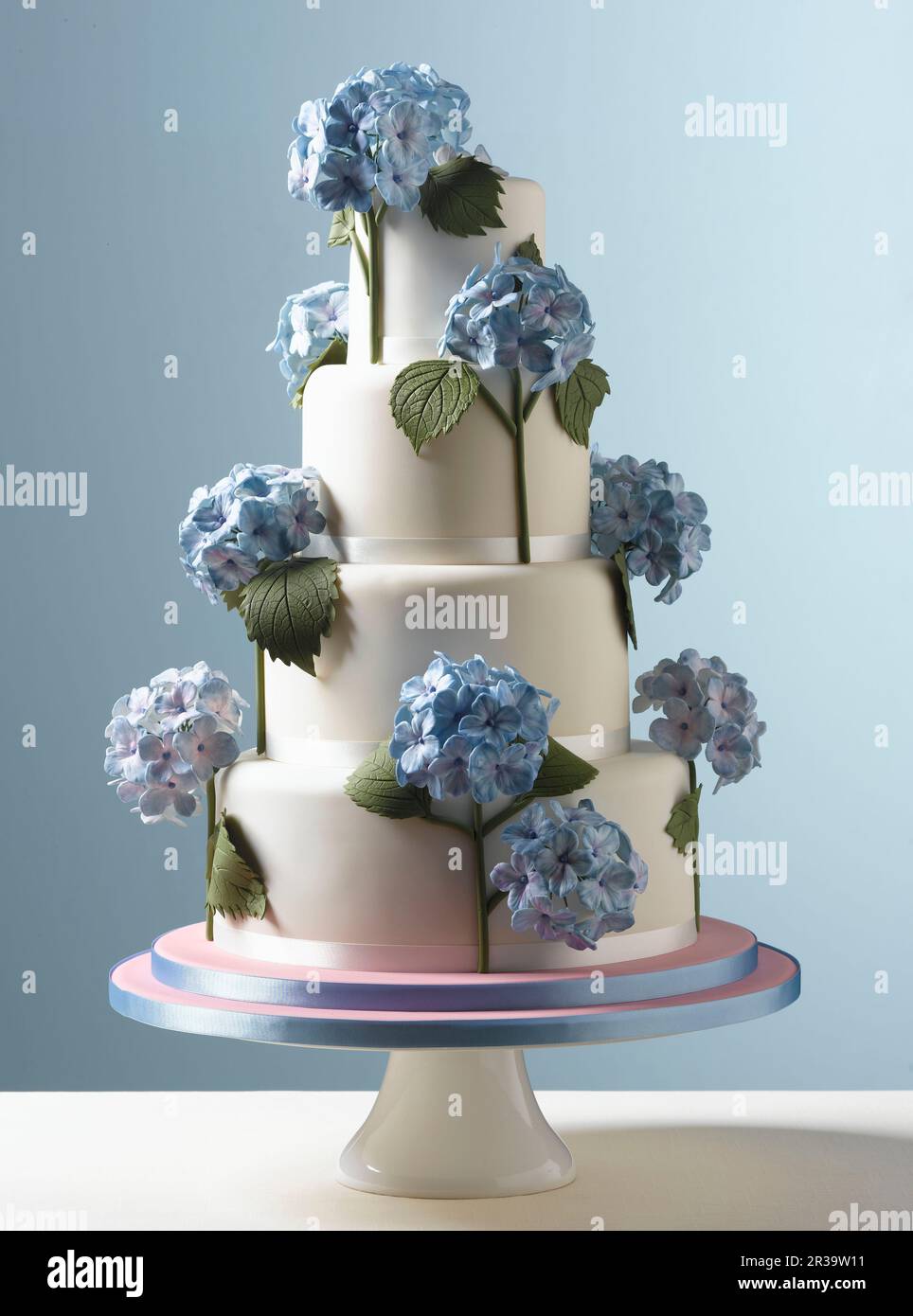 Easter Celebrations, tiered white wedding cake with blue hydrangea flowers with a pale blue background Stock Photo