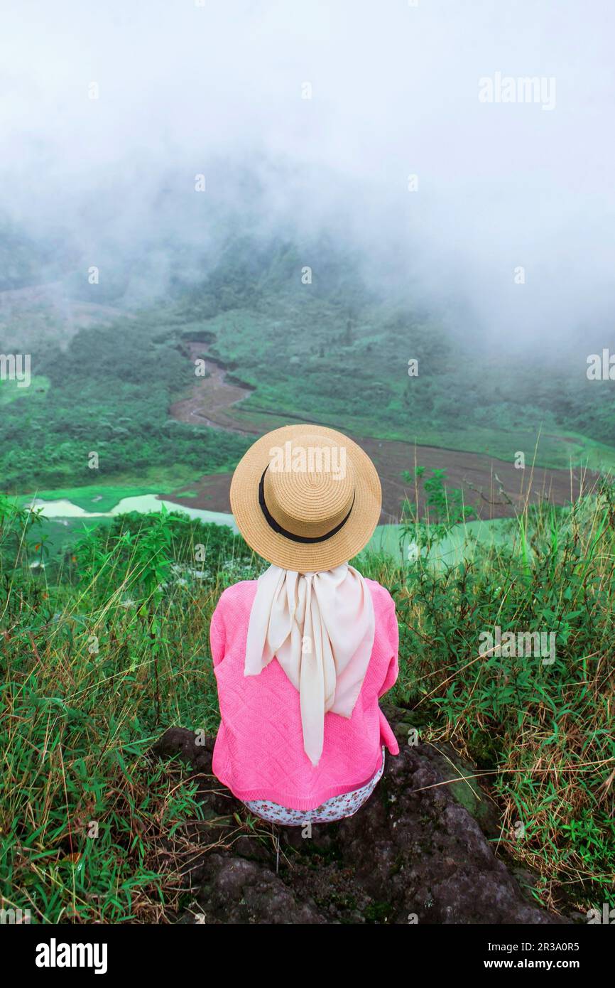 A female traveler sits enjoying the beauty of nature from above the mountains Stock Photo