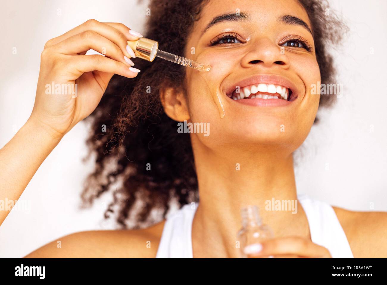 Cute smiling african young woman applies moisturizing serum from ...
