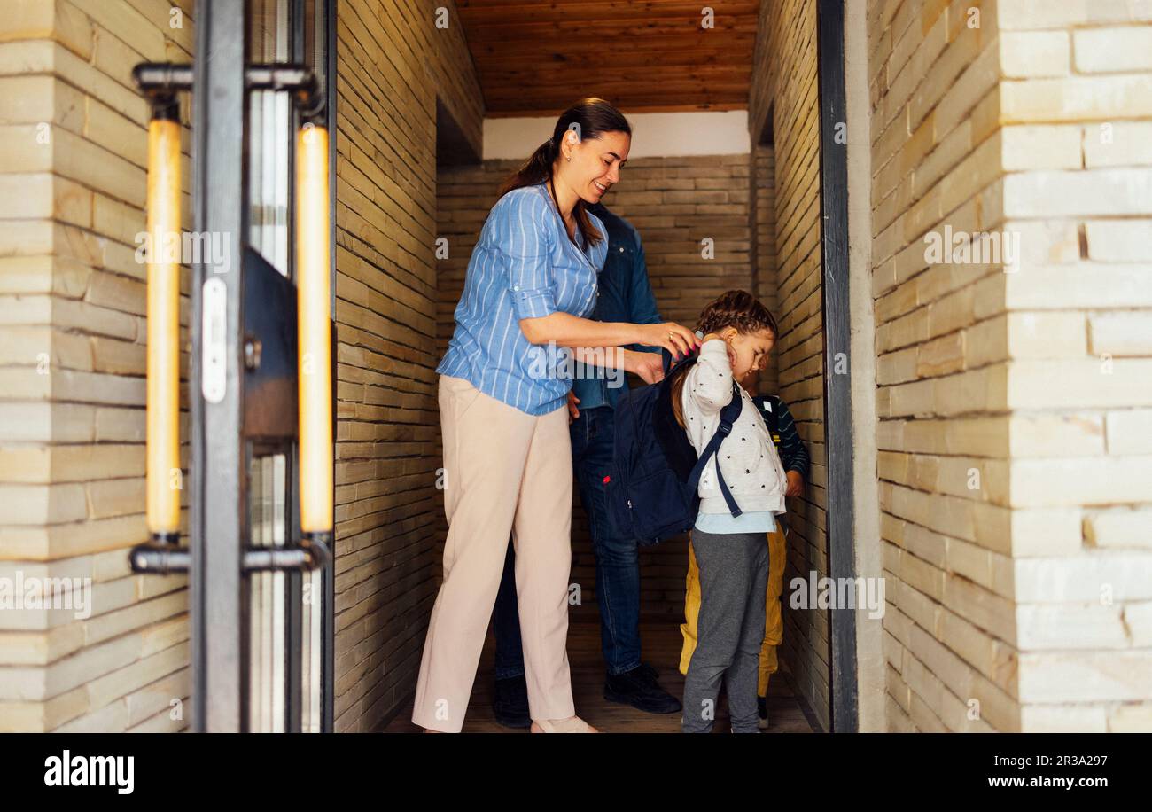Young parents seeing their cute kids off to school. Smiling mom, dad, daughter and son go down