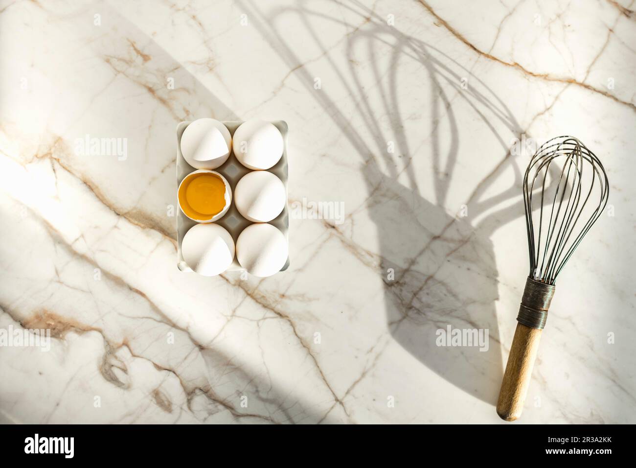 Eggs in an egg box, one open, next to a whisk Stock Photo