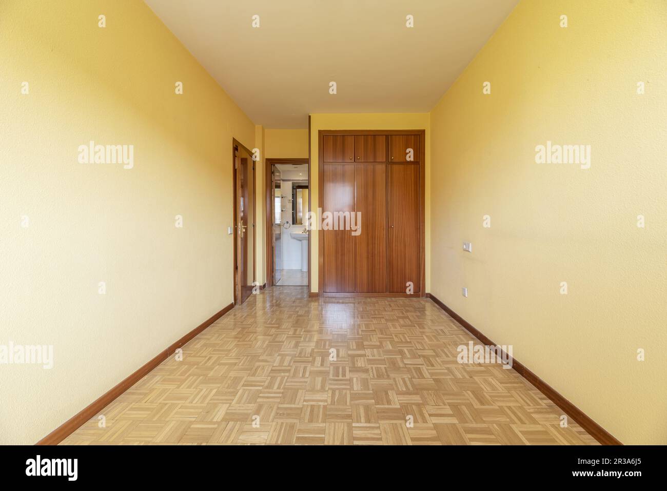 A spacious empty room with a built-in wardrobe with varnished sapele wood doors and an en-suite bathroom Stock Photo