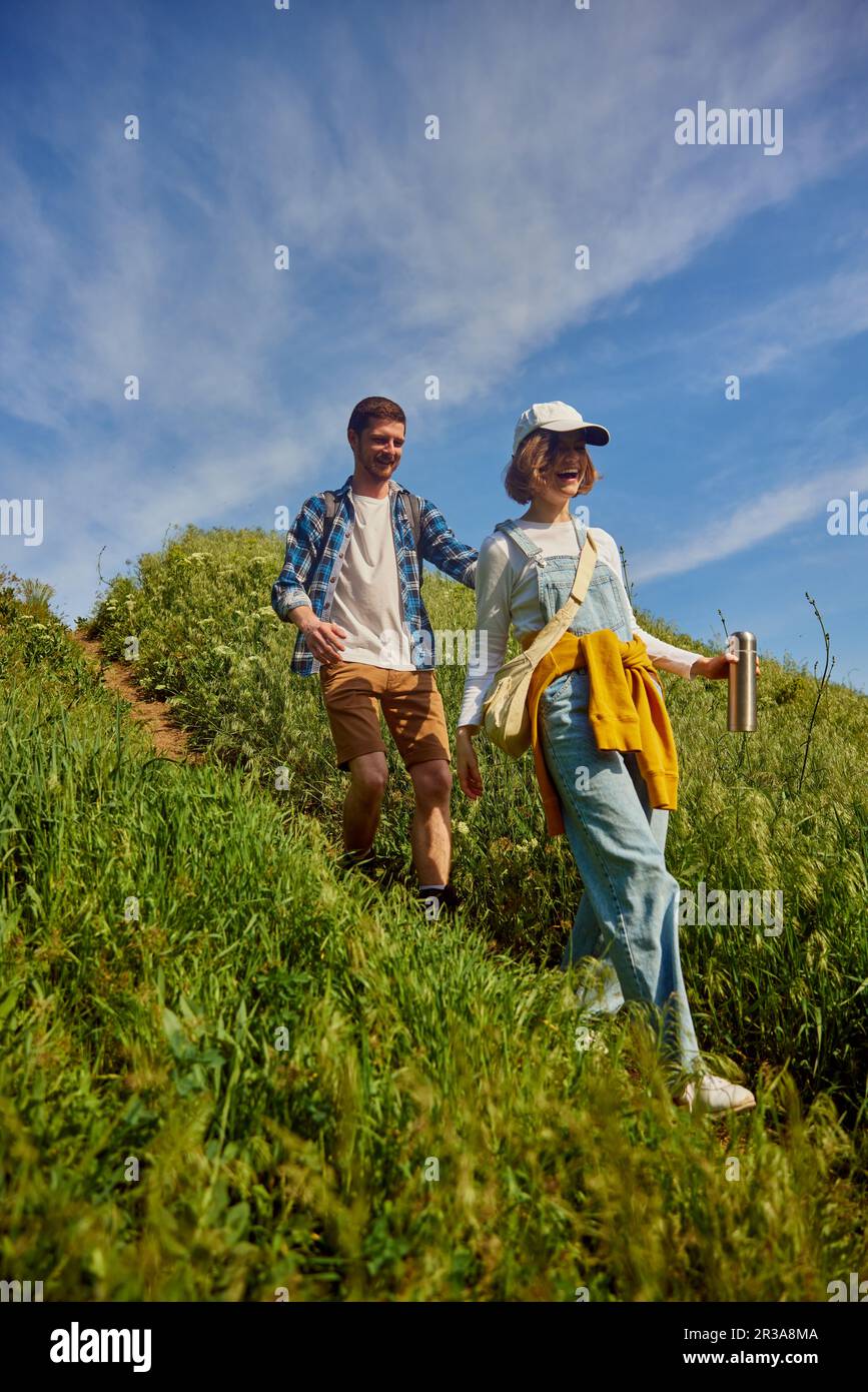 Happy, smiling friends, couple, young man and woman in casual clothes going hiking, walking down the hill on warm summer day Stock Photo