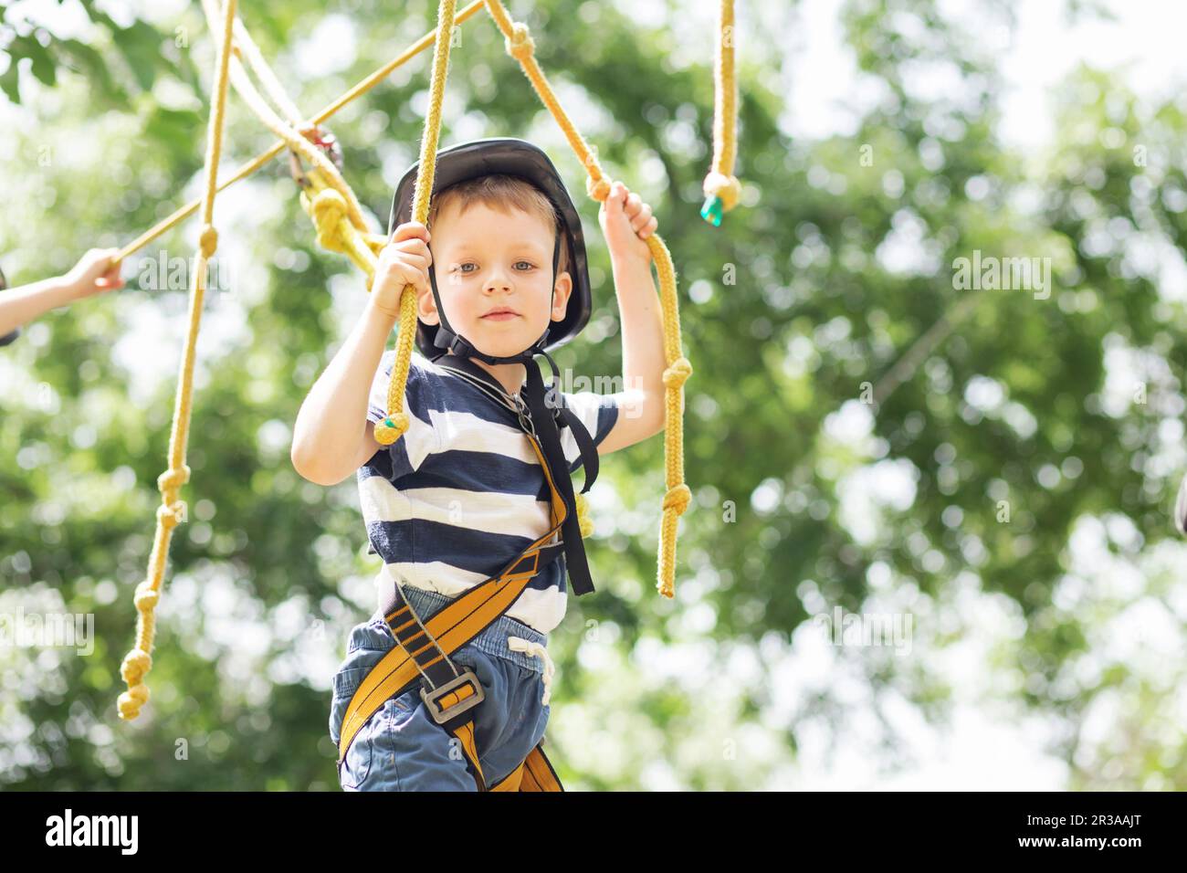 Kids climbing in adventure park. Boy enjoys climbing in the ropes course adventure. Child climbing h Stock Photo