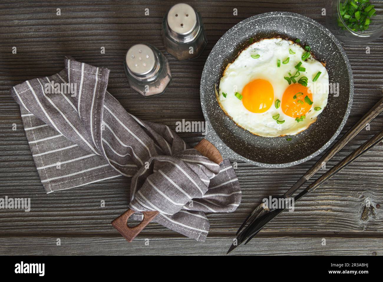 Fried eggs with green chives chopped for breakfast. Two fried eggs in a small pan on the dark wooden Stock Photo