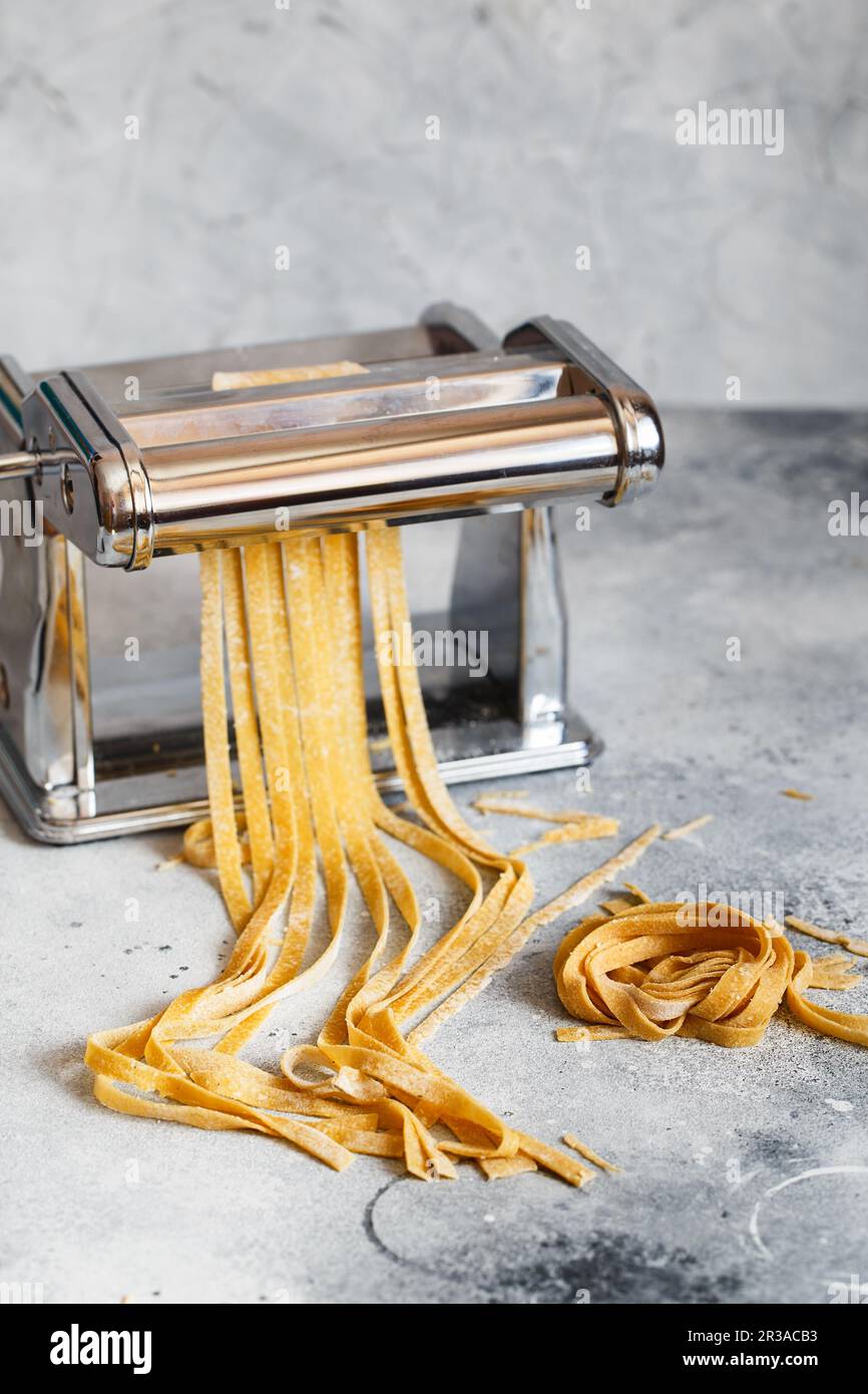Metal pasta maker with dough. Fettuccine coming out of a manual pasta