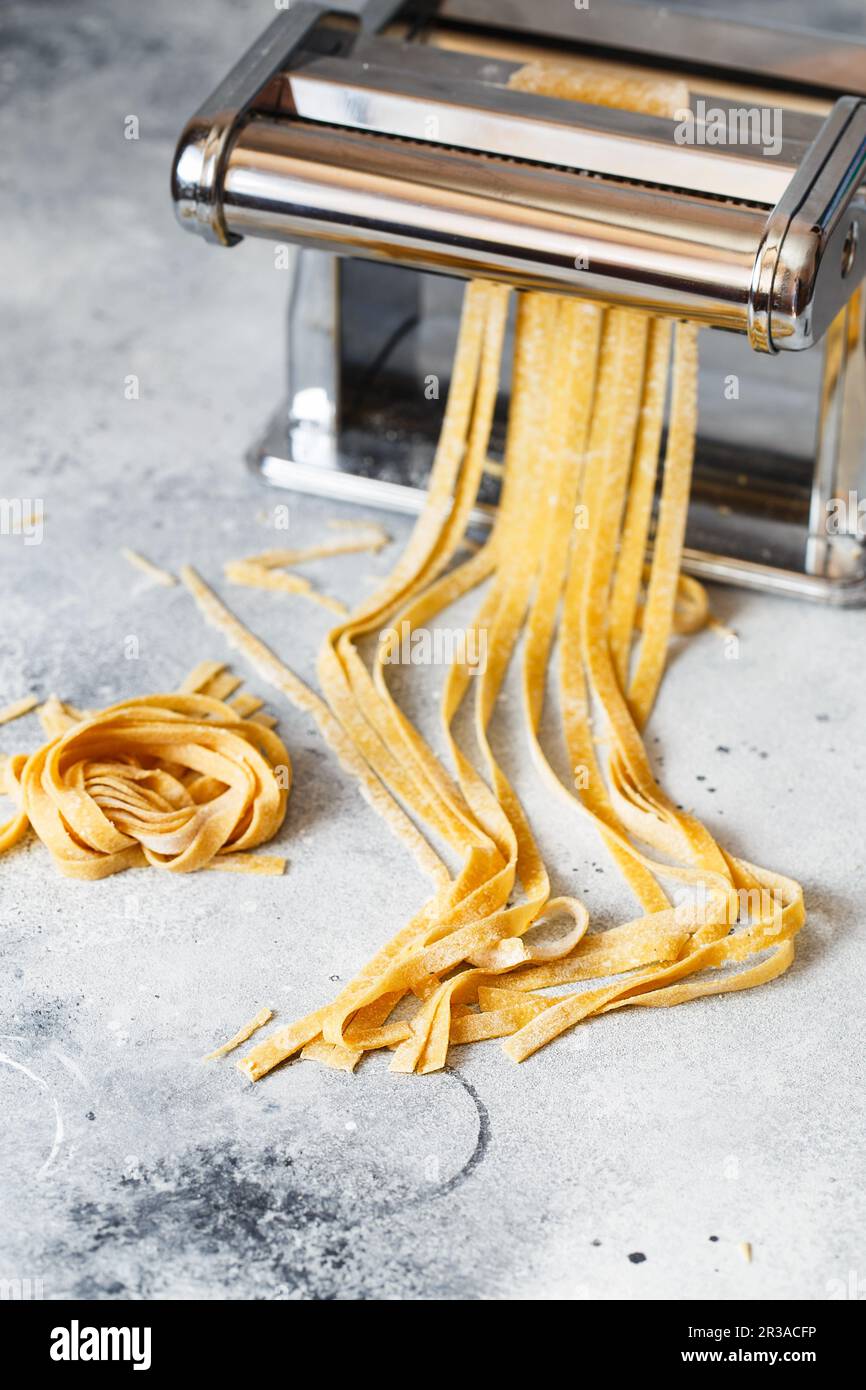 https://c8.alamy.com/comp/2R3ACFP/metal-pasta-maker-with-dough-fettuccine-coming-out-of-a-manual-pasta-machine-making-noodles-with-p-2R3ACFP.jpg