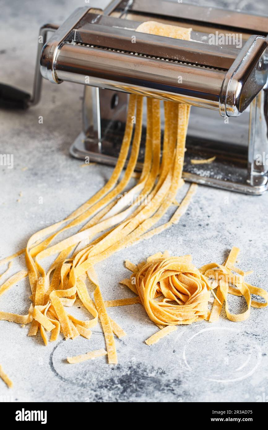 https://c8.alamy.com/comp/2R3AD75/metal-pasta-maker-with-dough-fettuccine-coming-out-of-a-manual-pasta-machine-making-noodles-with-p-2R3AD75.jpg