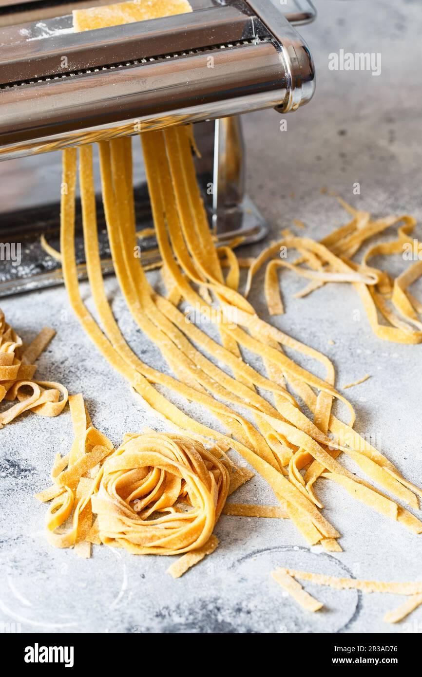 https://c8.alamy.com/comp/2R3AD76/metal-pasta-maker-with-dough-fettuccine-coming-out-of-a-manual-pasta-machine-making-noodles-with-p-2R3AD76.jpg
