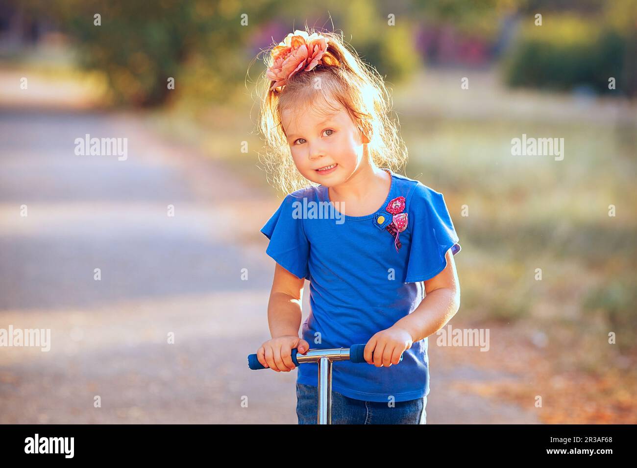 Portrait of playful fun smiling little girl with scooter in the soft light of evening sun Stock Photo