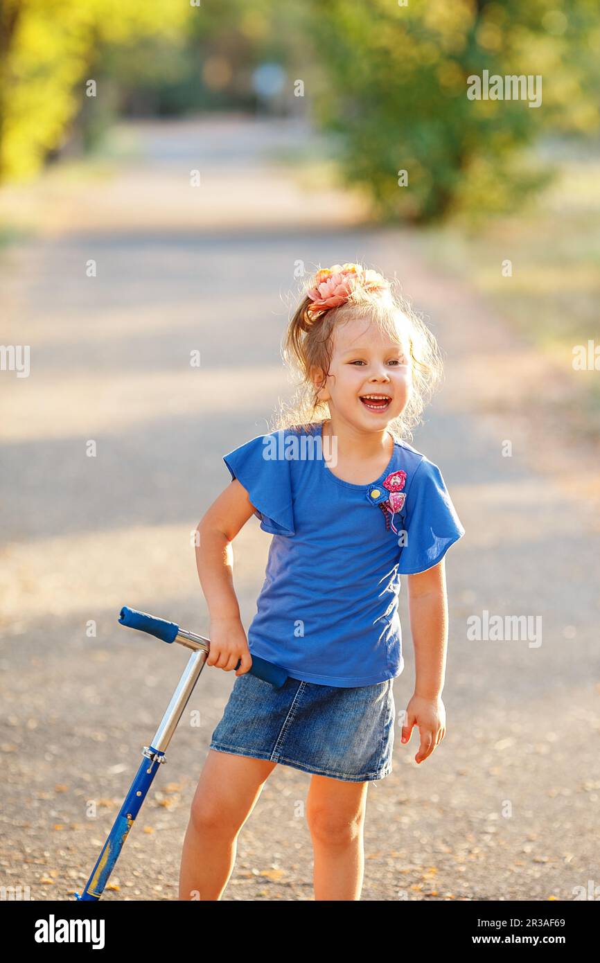 Portrait of playful fun smiling little girl with scooter in the soft light of evening sun Stock Photo