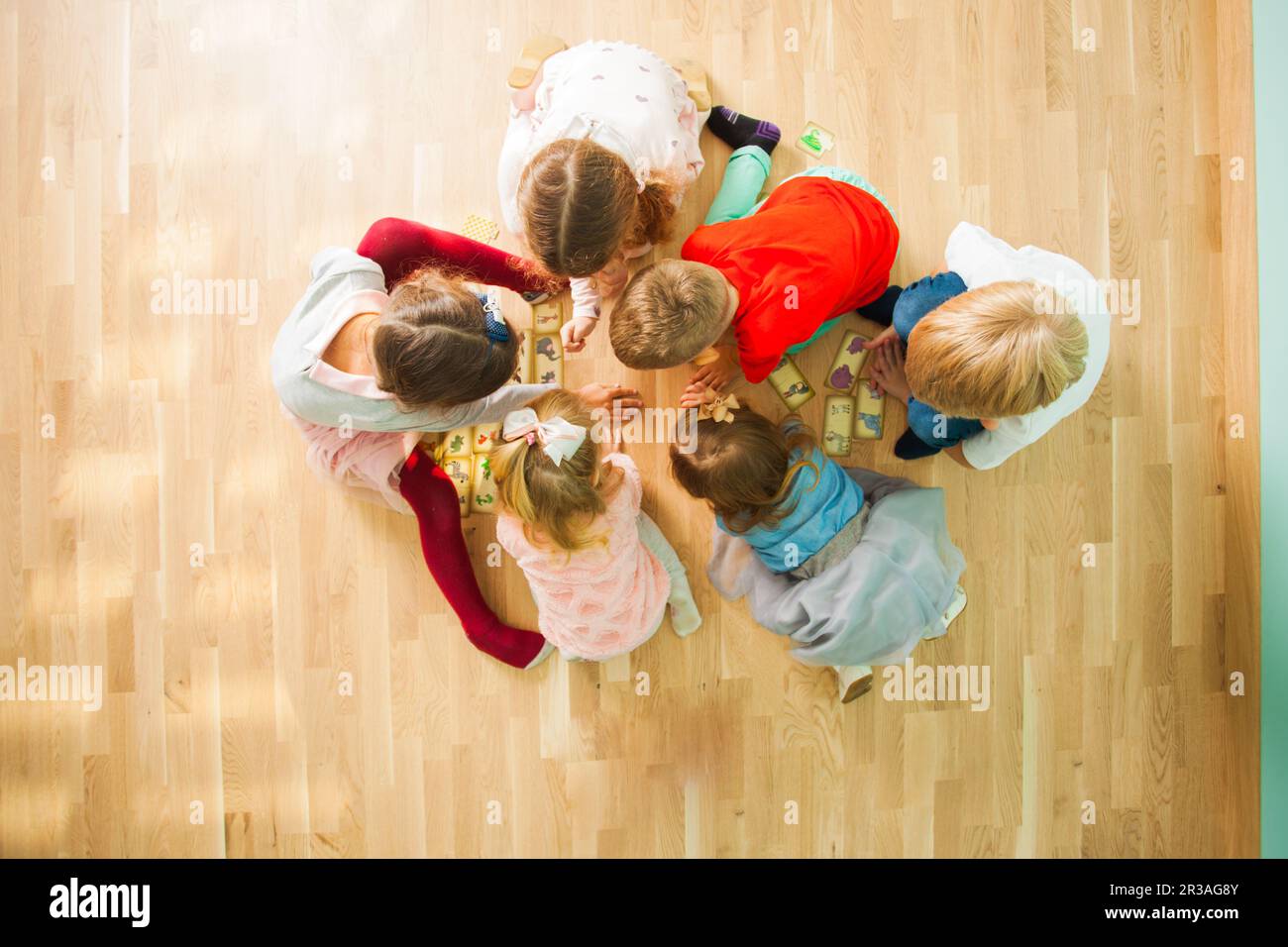 Group of children playing educational cards on a floor. Puzzle with animals mother and baby. Stock Photo