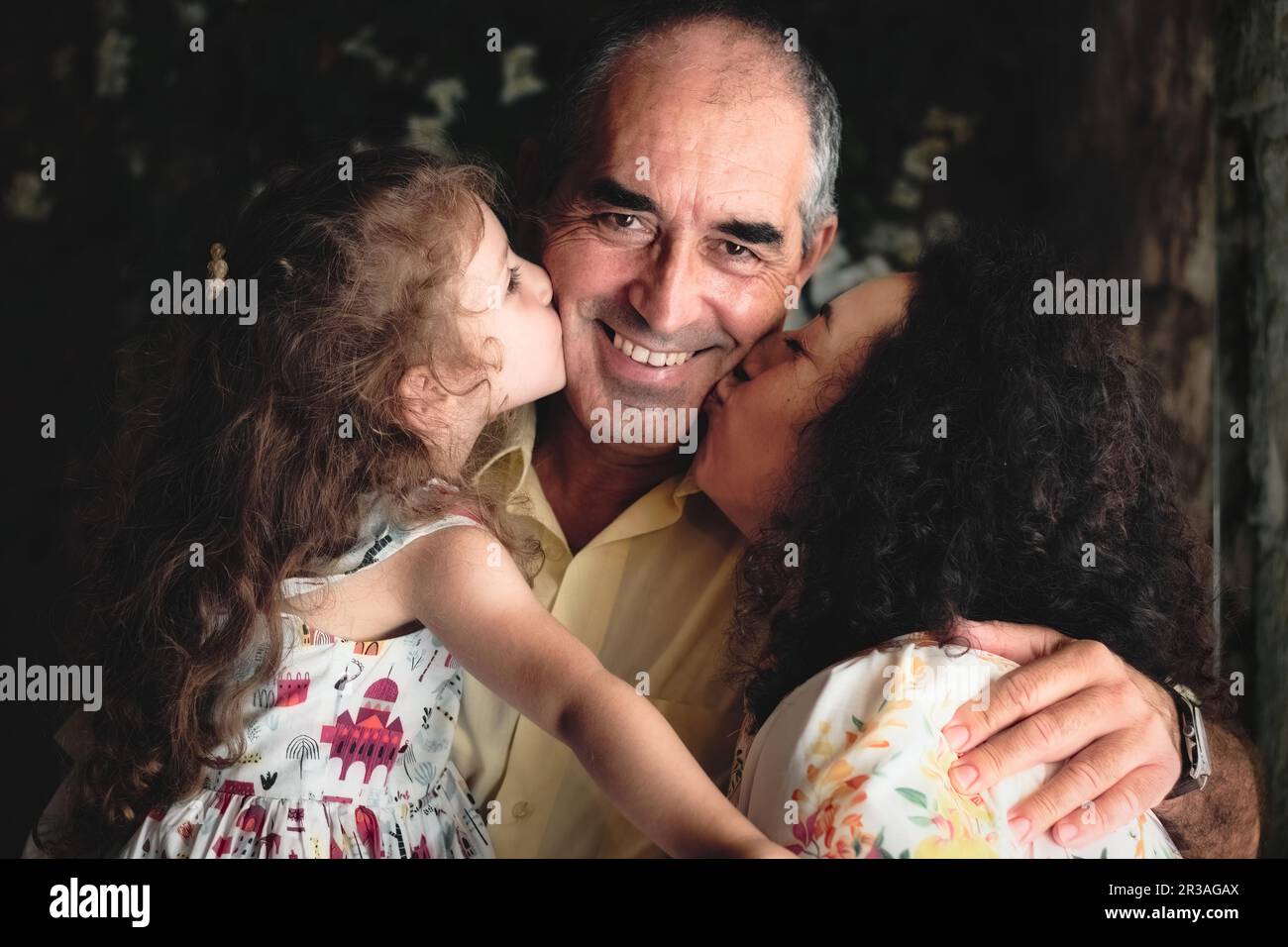 3 generations lifestyle portrait shot - a woman and her daughter kissing the father / grandfather looking at the camera - white Caucasian family celeb Stock Photo