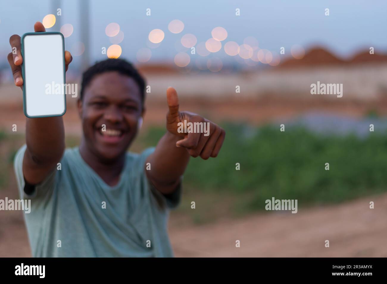 portrait of excited African boy holding a smartphone with white black screen with his hand, with his thumbs up. mobile phone with empty space, copy sp Stock Photo
