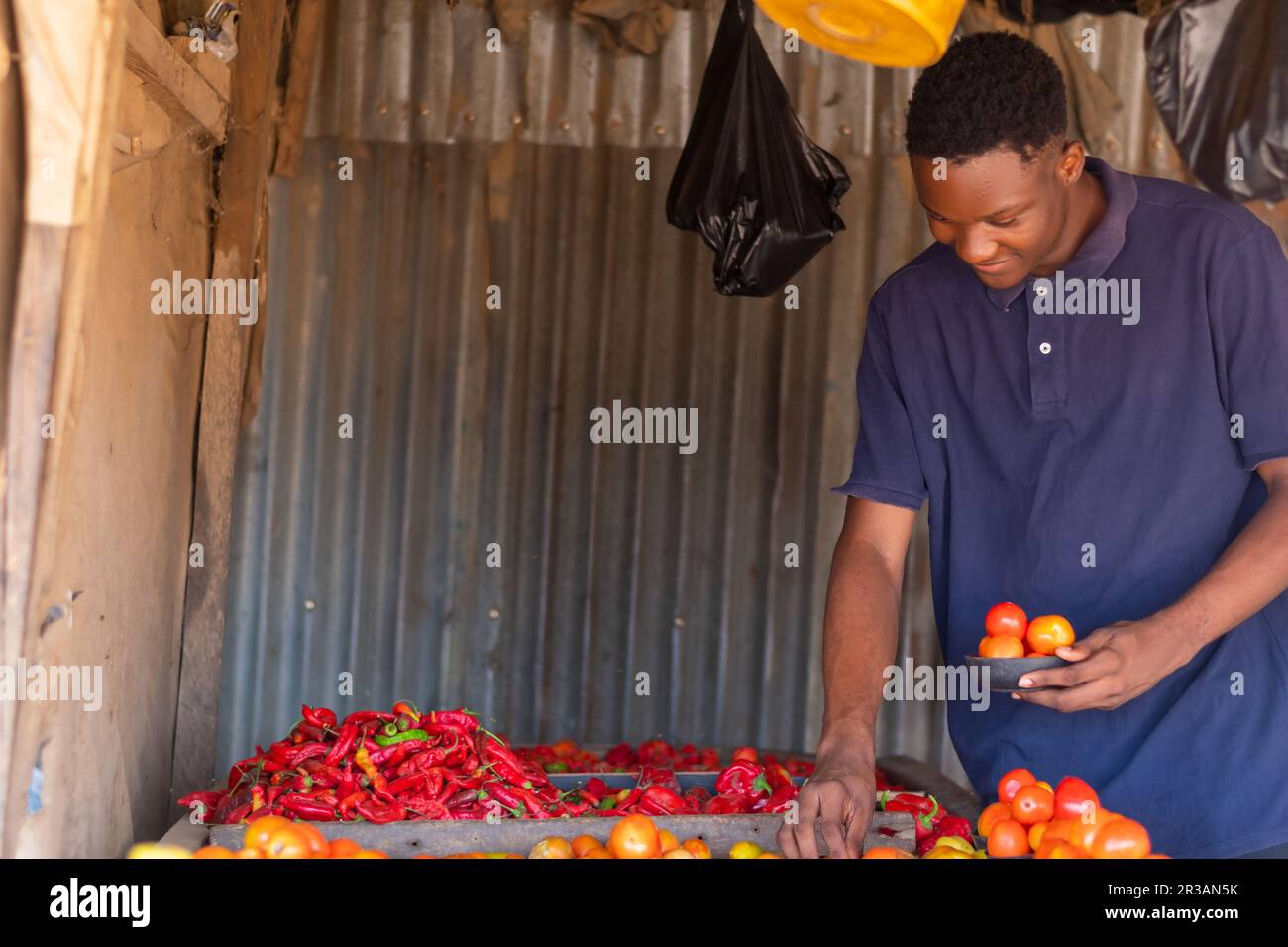 young handsome african local trader feeling happy has he arranges tomatoes for sale. Stock Photo