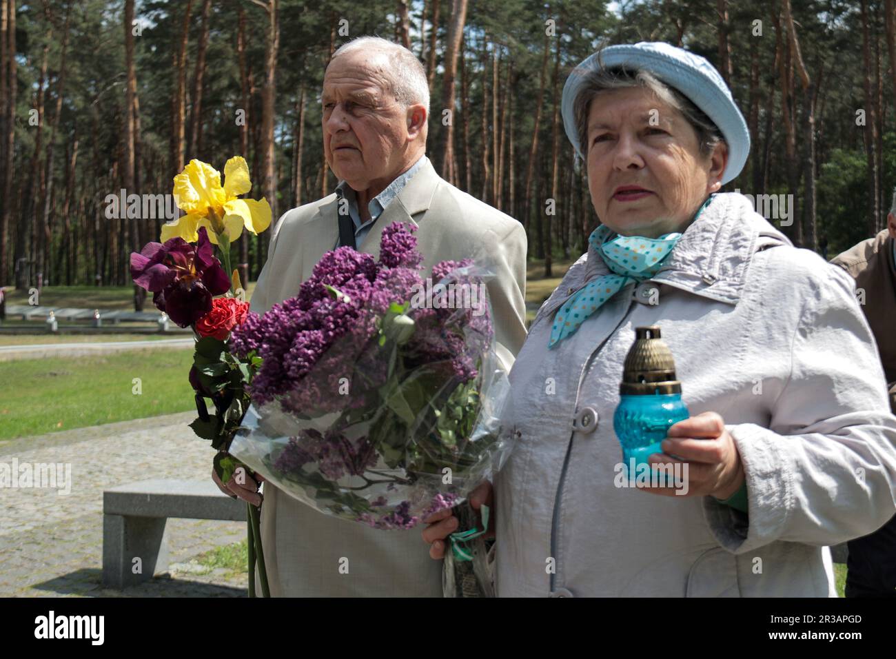 KYIV, UKRAINE - MAY 21, 2023 - A senior man and woman hold flowers and a vigil lantern at the Bykivnia Graves National Historical and Memorial Reserve Stock Photo