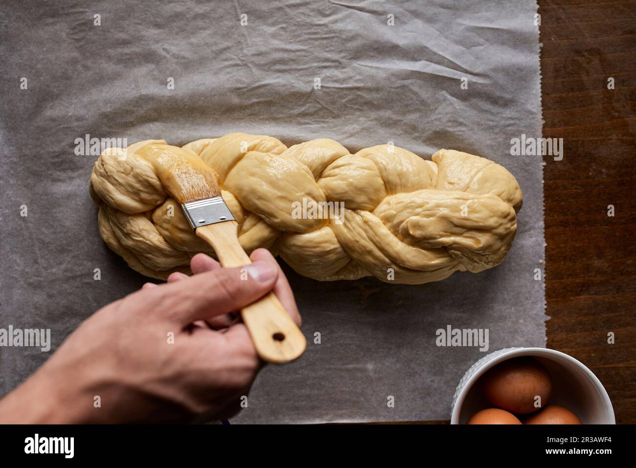 A braided loaf being spread with egg yolk Stock Photo