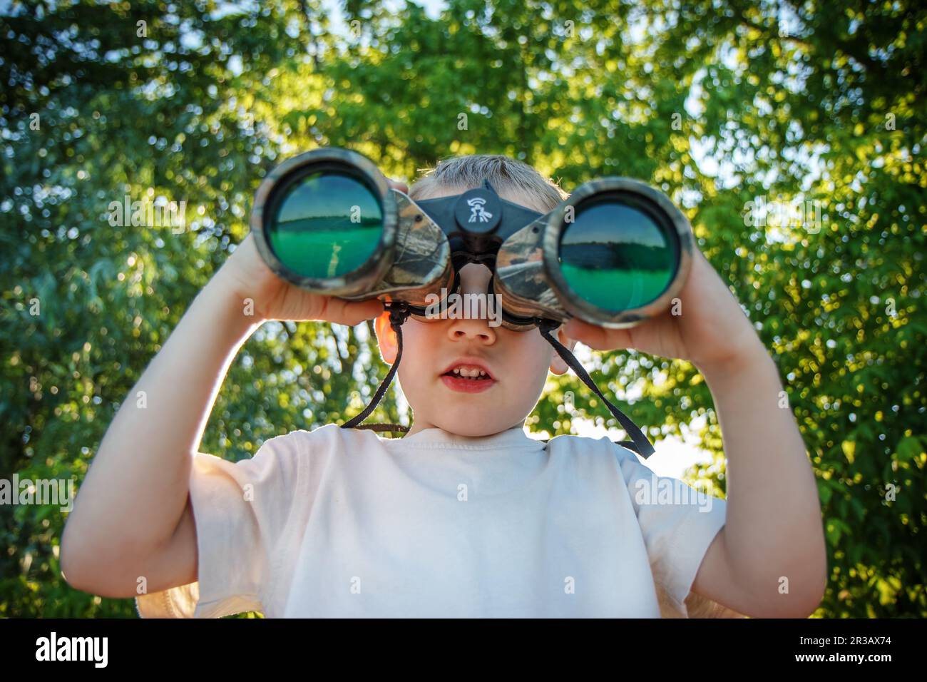 Little boy looking through binoculars on river bank Stock Photo
