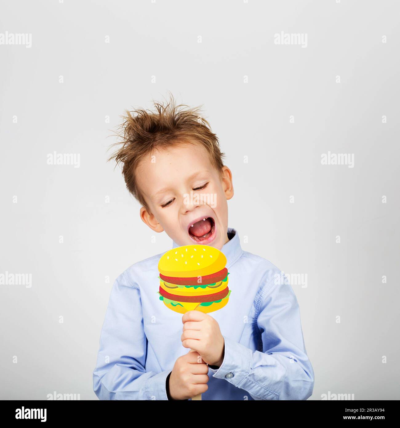 Cute little school boy with fake paper burger against a white