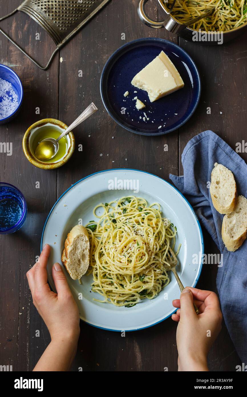 Spaghetti with garlic, parsley, chilli, olive oil and parmesan, bread, permesan cheese, olive oil, water in a glass, salt Stock Photo