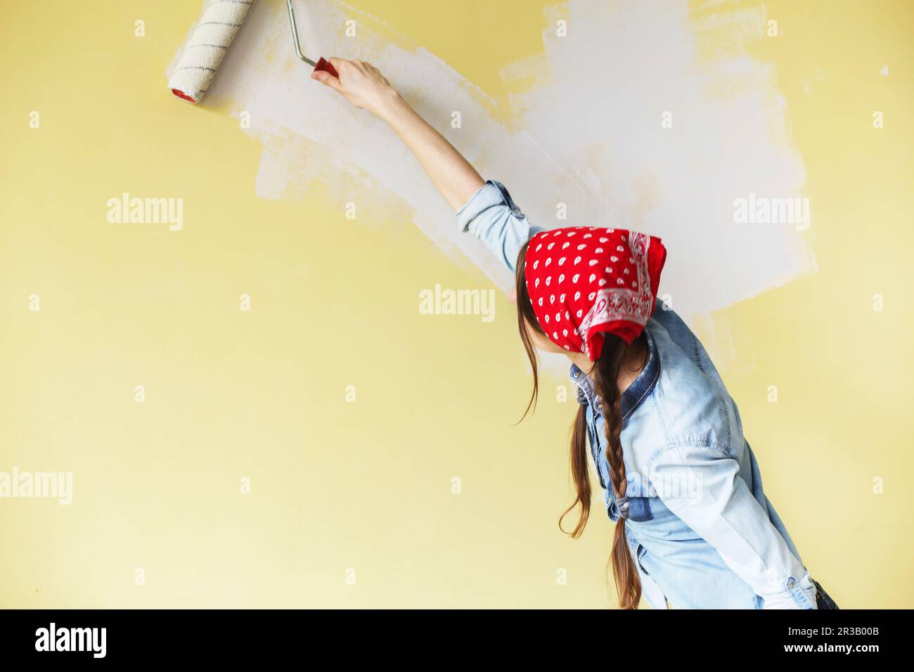 Beautiful girl in red Headband painting the wall with paint roller
