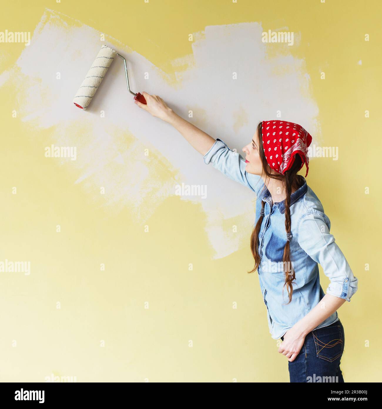 Beautiful girl in red Headband painting the wall with paint roller