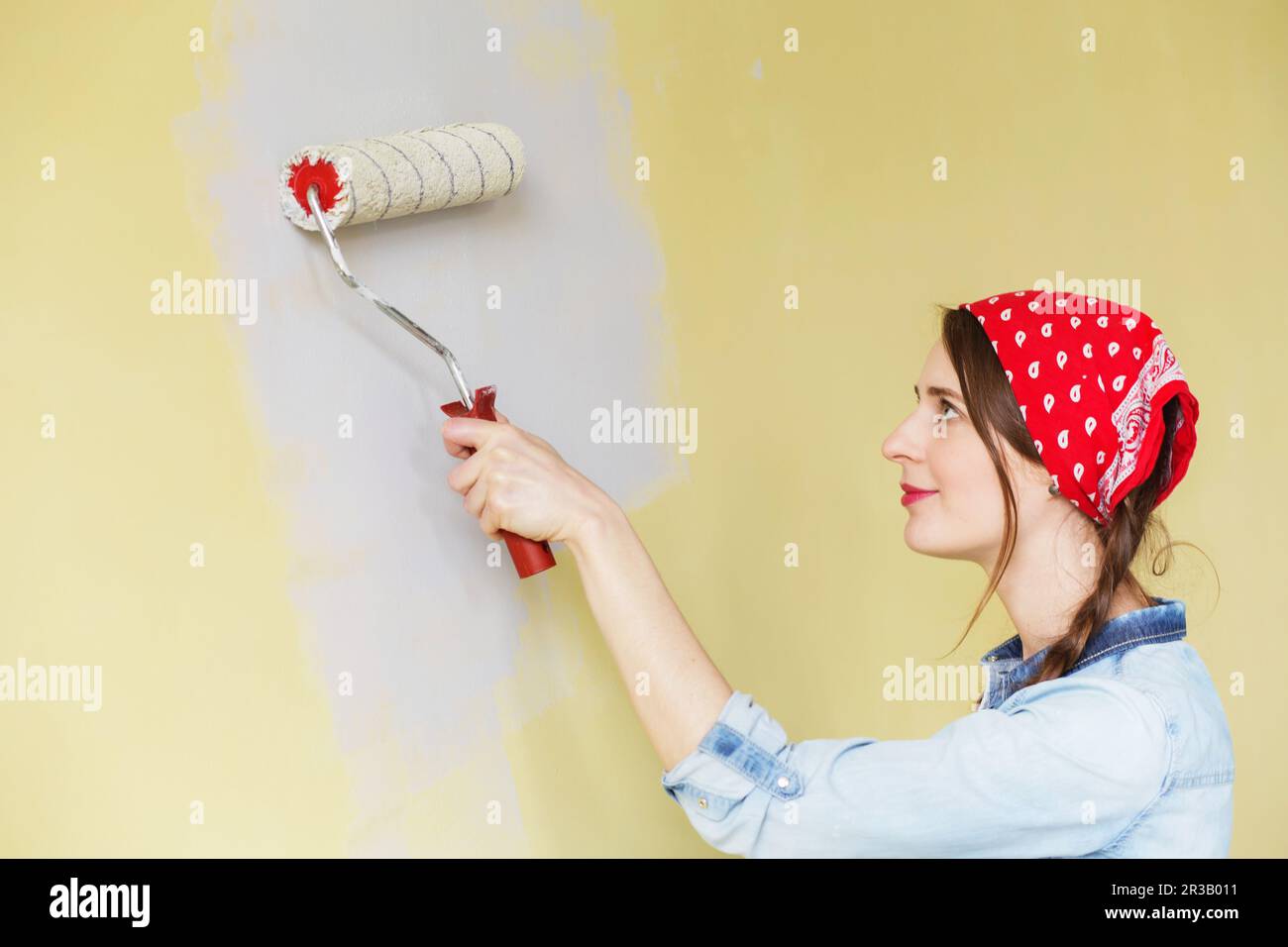 Beautiful girl in red Headband painting the wall with paint roller