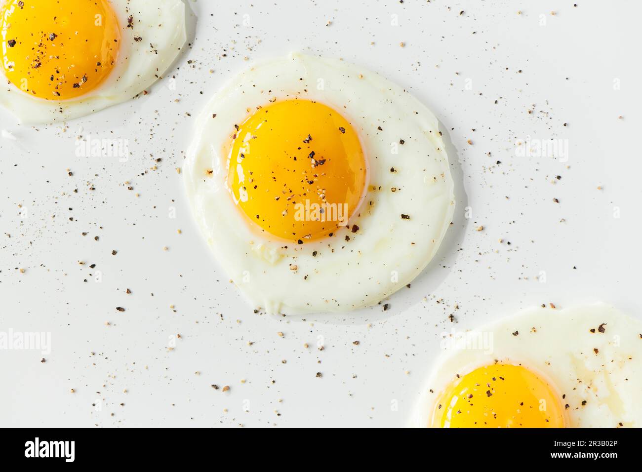 Three sunnyside eggs with pepper sprinkled over top Stock Photo