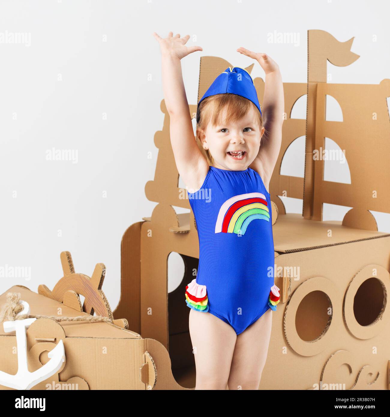 Cute Little girl wearing bright swimsuit playing with cardboard ship on white background. Happy chil Stock Photo