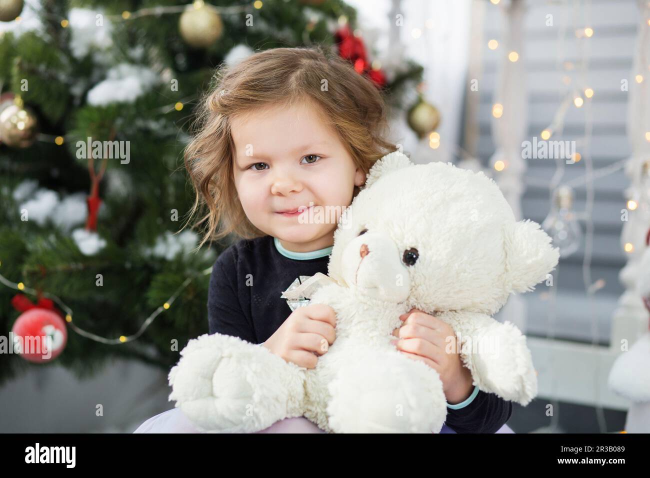 Portrait of a cute little girl hugging a soft teddy bear in interior with Christmas decorations Stock Photo