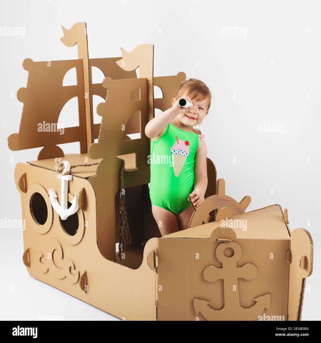 Cute Little girl wearing bright swimsuit playing with cardboard ship on white background. Happy chil Stock Photo